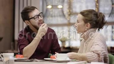 <strong>一个</strong>年轻人正在餐馆里用<strong>勺子</strong>喂妻子吃蛋糕